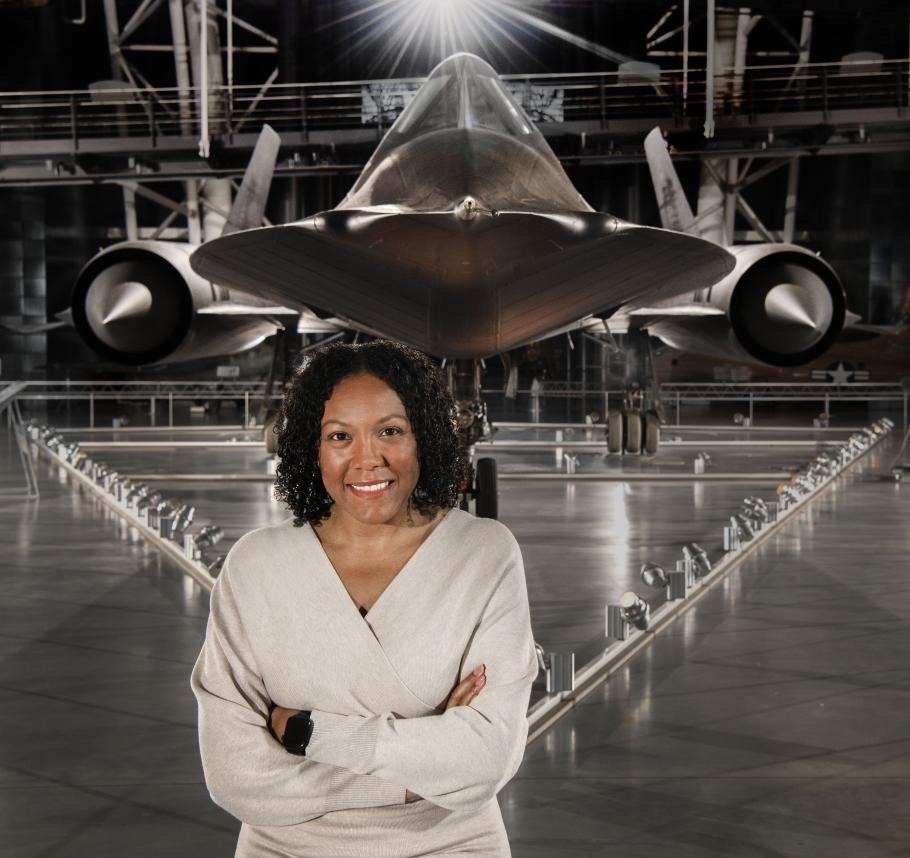 A woman stands in front of a large black airplane.
