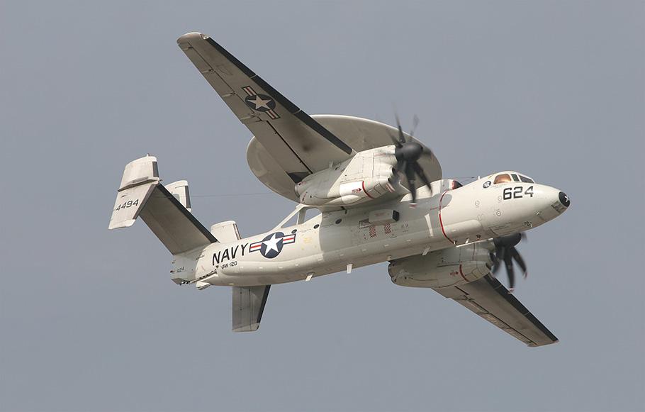 A white, twin-turboprop airplane flies against a gray sky during daylight. The airplane has U.S. Navy markings.