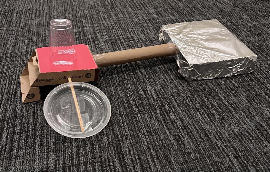 Recycled materials  taped together to look like a space station. They consist of a cardboard box wrapped in aluminum foil, a food container cover taped to a chopstick, a paper tube, a plastic cup and an empty coffee filter box.