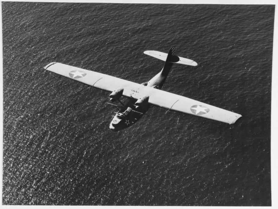 Black and white image of a small aircraft viewed from above flying over water.
