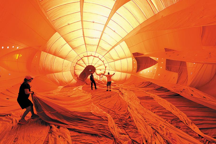 Three people stand inside one balloon's cavernous orange envelope during inflation.