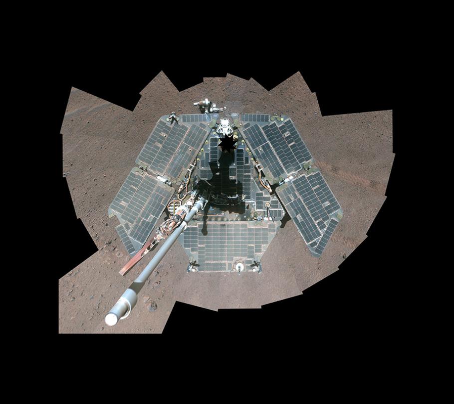 A rover on the dull red surface of Mars, photographed from above, with three large solar panels mounted in a triangular configuration on its sides.