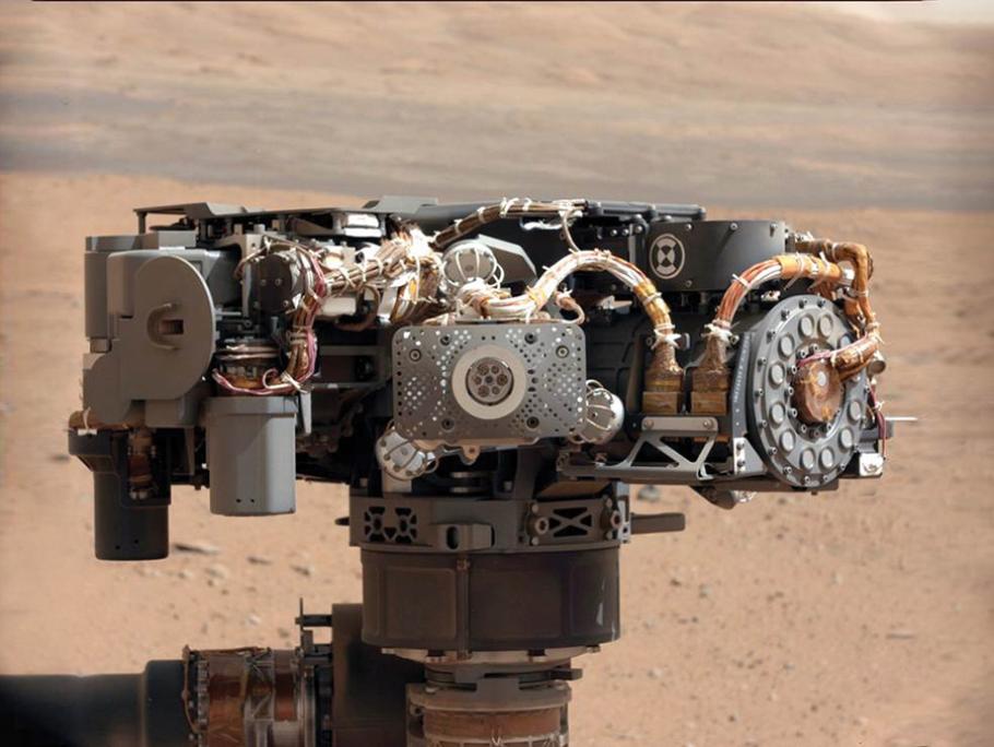 Instruments and thick cables stand  at the top of a pole mounted on a rover, with red Martian desert landscape in the background.