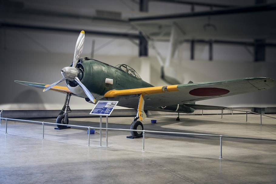 A single-propellar photo, painted dark green with some yellow highlights and Japanese markings visible on its right wing sits on display at a museum.