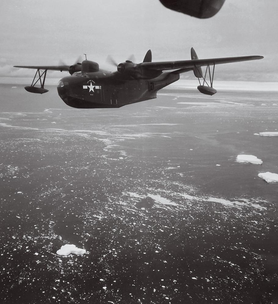 A black-and-white photo shows a massive-looking aircraft with two propellars and a wide fuselage flying over ocean covered in small icebergs.