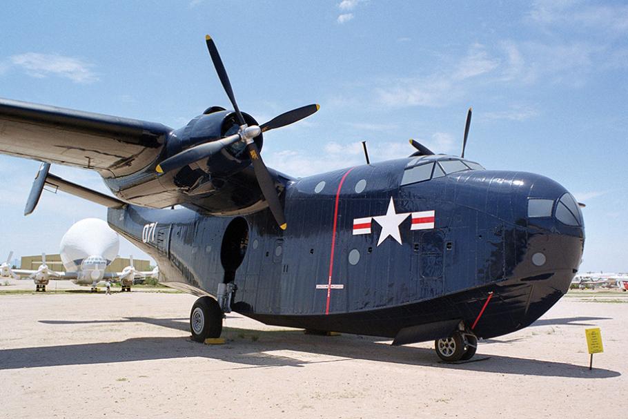 A massive-looking aircraft with two propellars and a wide fuselage is painted dark blue with U.S. Air Force markings. It's parked on a concrete tarmac with blue sky above.