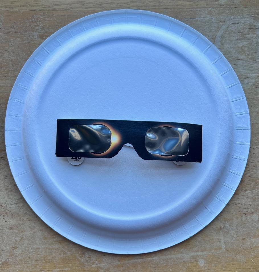 A pair of eclipse glasses sits on the back of a paper plate.