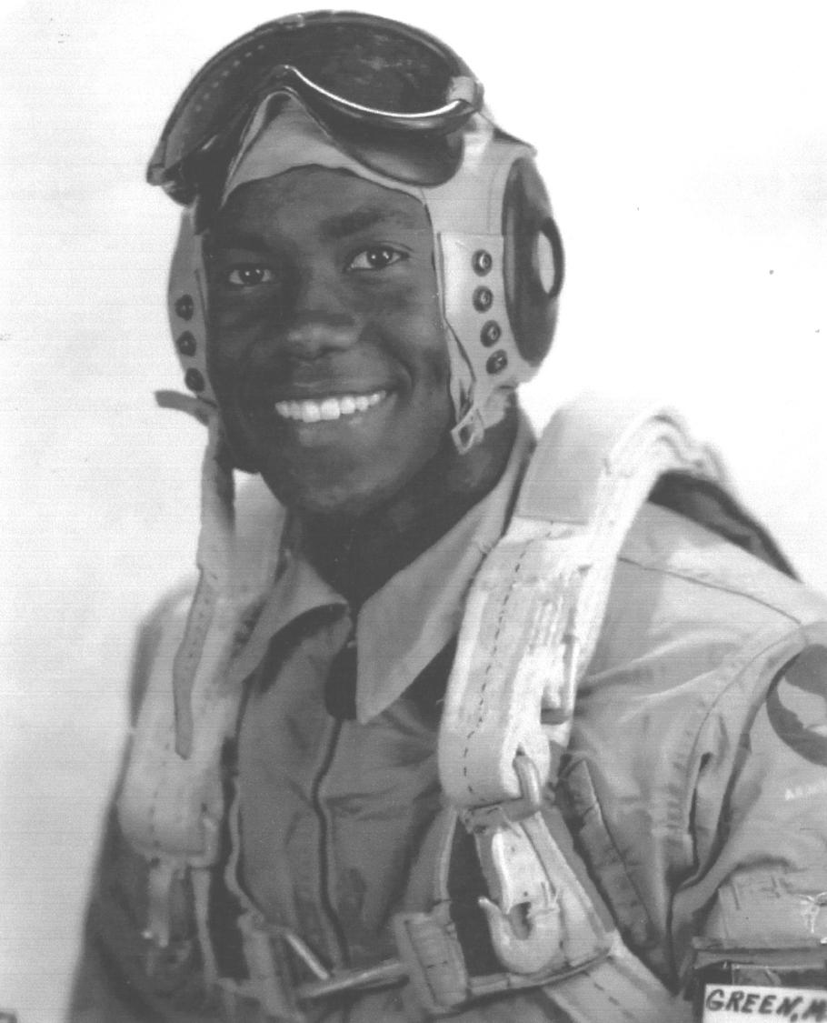 A man poses for a portrait wearing a flight cap and goggles and a flight suit.