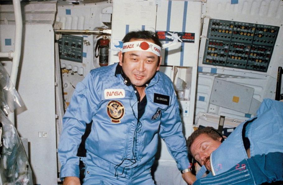 Ellison Onizuka onboard a spacecraft in space while wearing a flight suit and a bandana.