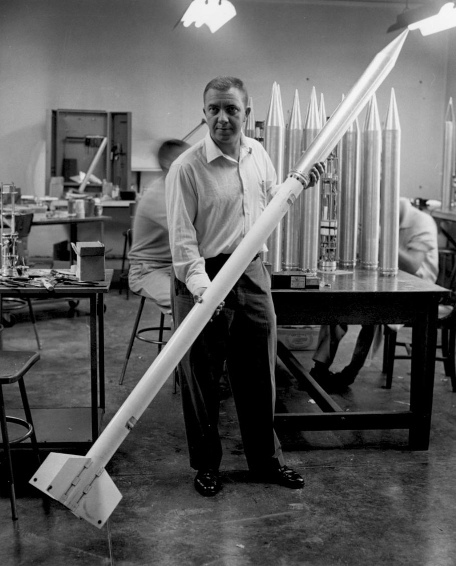 Man holding a rocket that is the size of him in an interior facility.