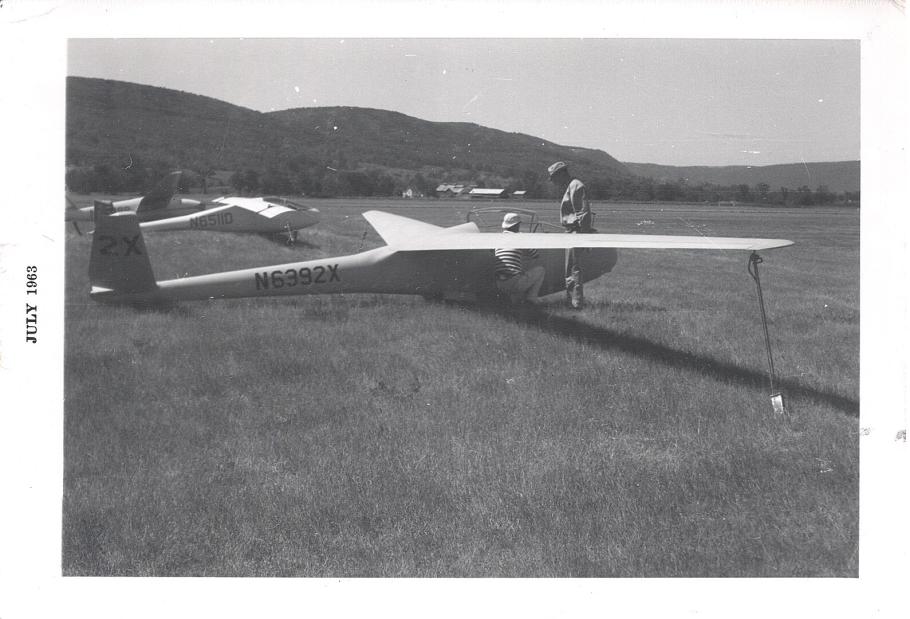 A man standing by a sailplane in a grass field.