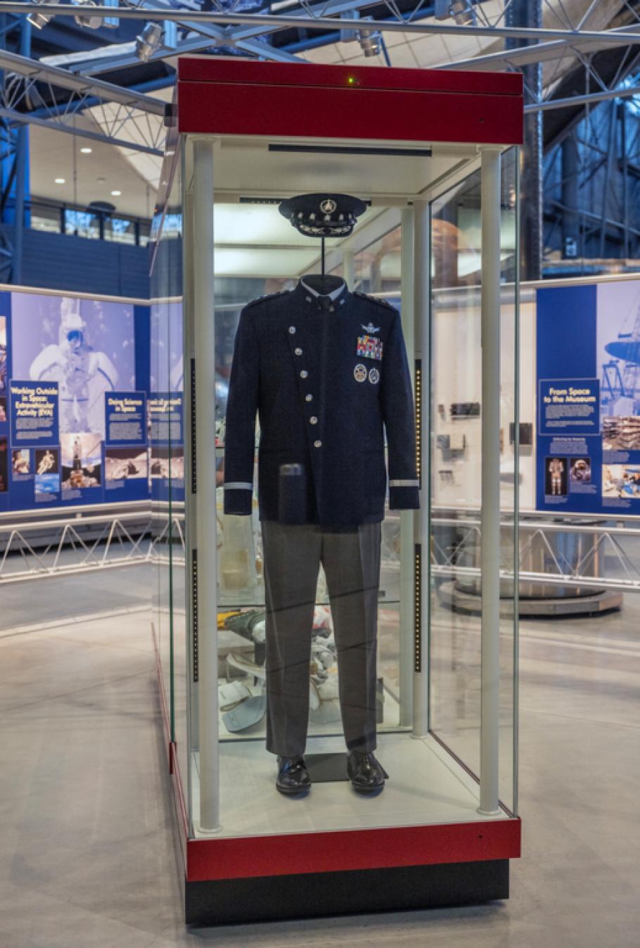 A space themed military uniform on display in a glass enclosure at a museum.