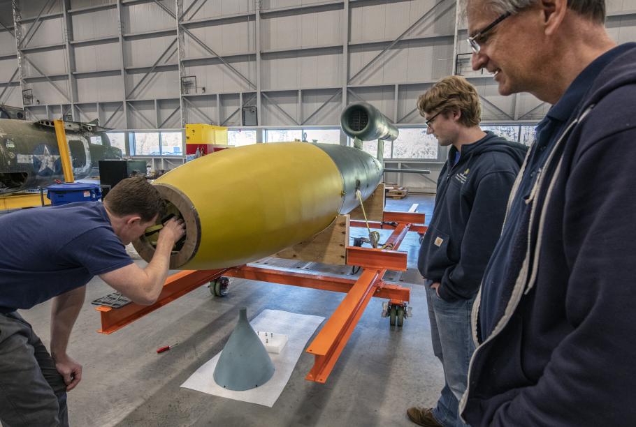 Three men inspect a missile in a restoration hangar.