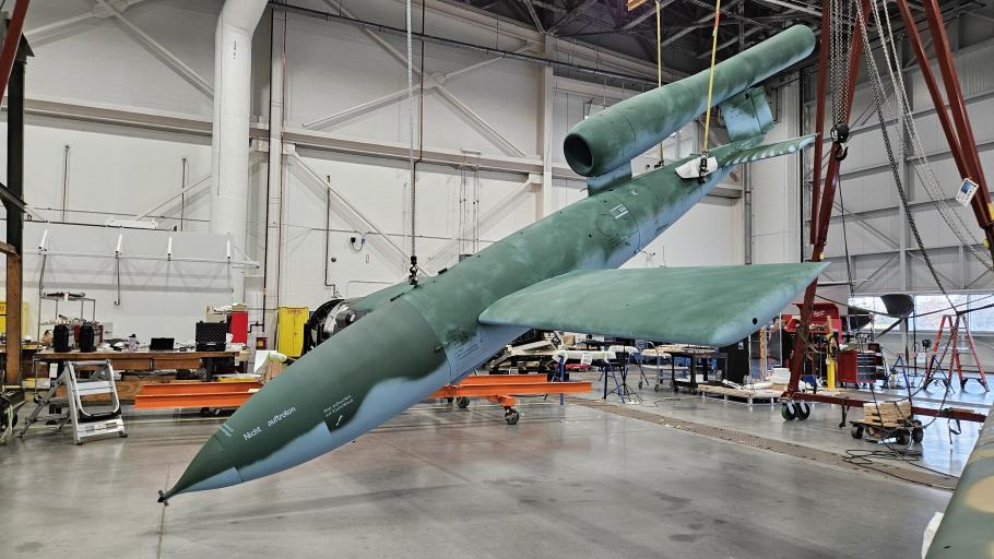 A missile with fresh new paint hangs diagonally from the ceiling in a hangar.