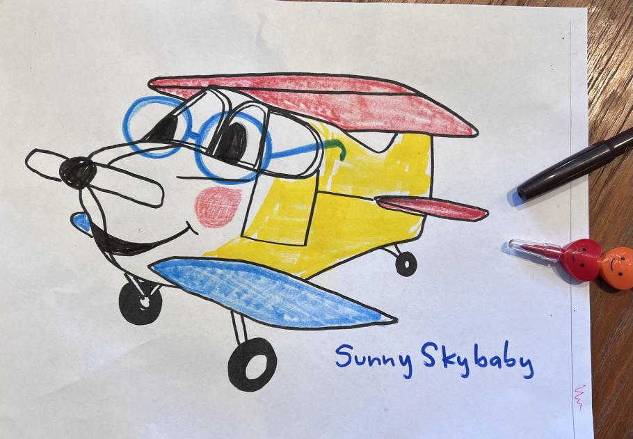 Drawing of a colorful cartoon airplane with a cheerful expression. Handwritten at the bottom on the page is the name Sunny Skybaby.