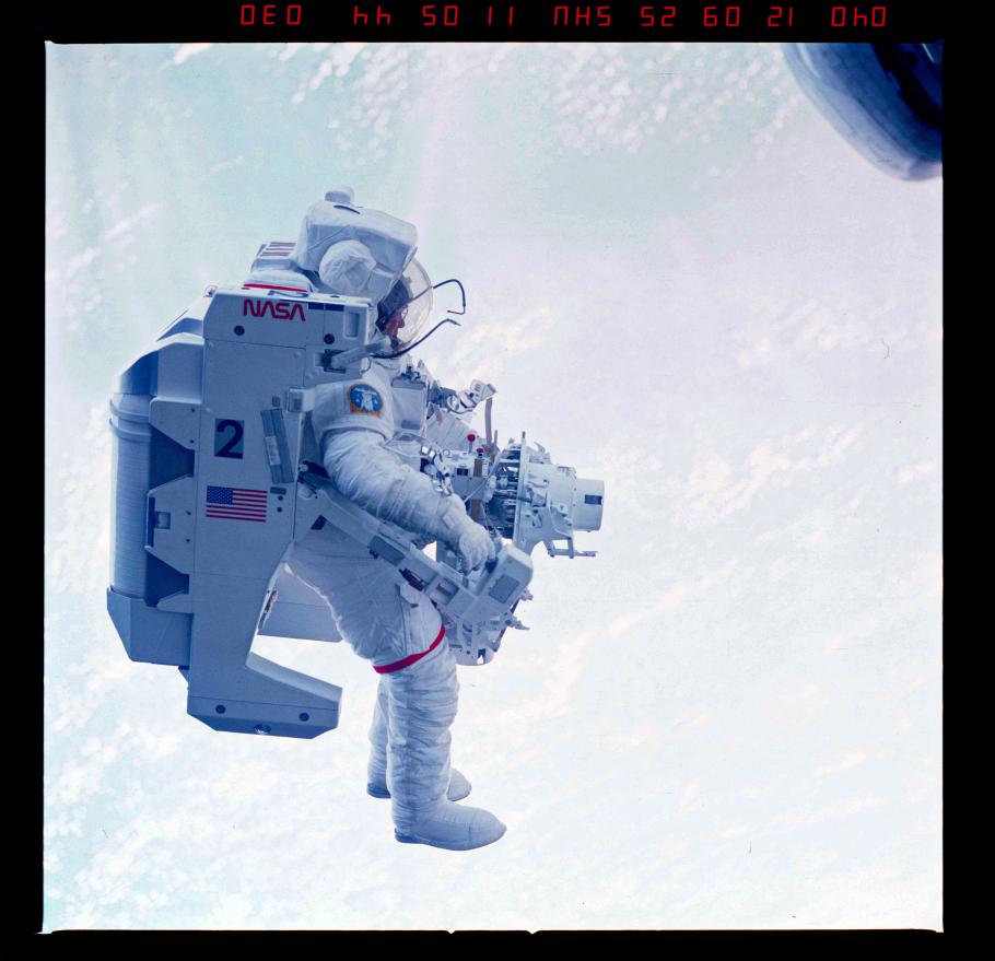 An astronaut equipped with a jetpack floats in outer space with distant earthly cloud in the background..