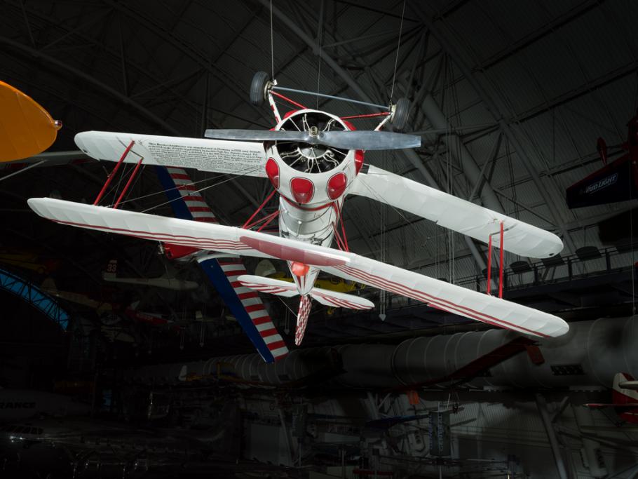 White and red painted single-engine aerobatic and military trainer biplane hanging in the museum.