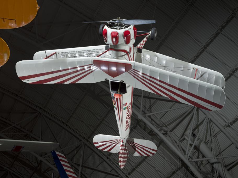 White and red painted single-engine aerobatic and military trainer biplane hanging in the museum.