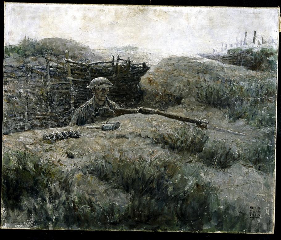 Man in military uniform looks out from a trench. 