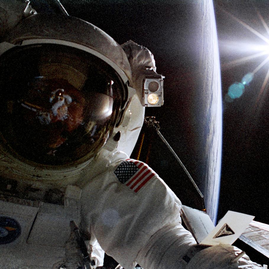 A photograph of an astronaut in his space suit, with a large spherical shape in the background.