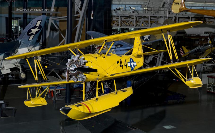 Bright yellow bi-plane with hand crank start hanging in the Steven F. Udvar-Hazy Center.