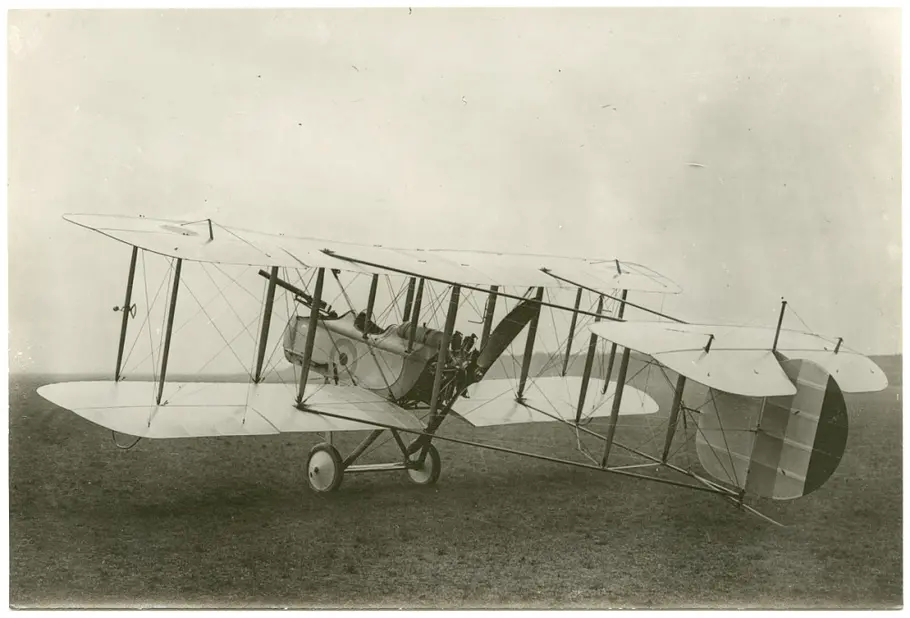A black and white photograph of a biplane with a long gun mounted to the front. 