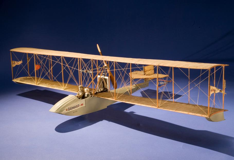 Wooden biplane-airboat model with space for two people, a passenger and the pilot. Flaglets are placed on the front structure in between the wings.