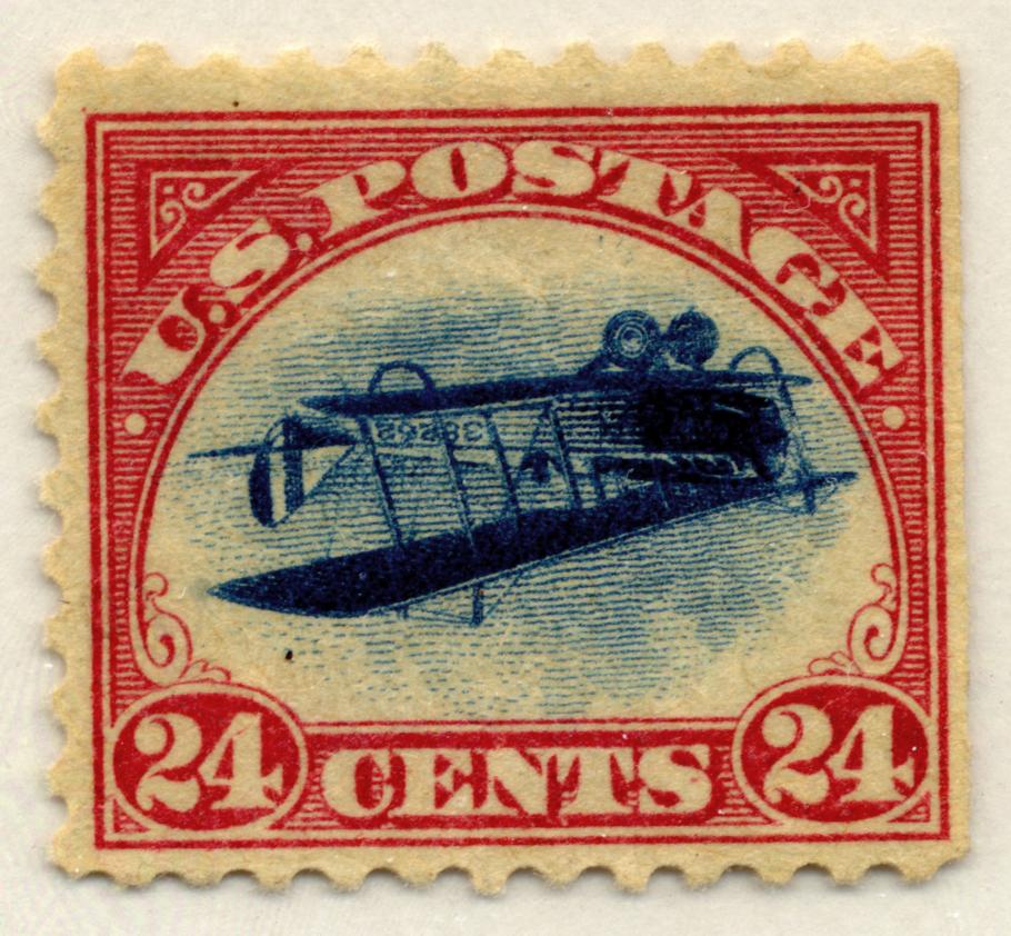 View of red, U.S. Air Mail postage stamp that has an error of the Jenny biplane facing upside down.