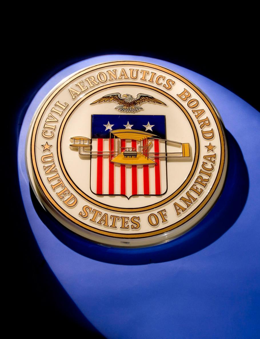 Golden-colored seal of the Civil Aeronautics Board featuring a red, white, and blue flag in the center below a bald eagle. The flag is covered in part by a yellow biplane.