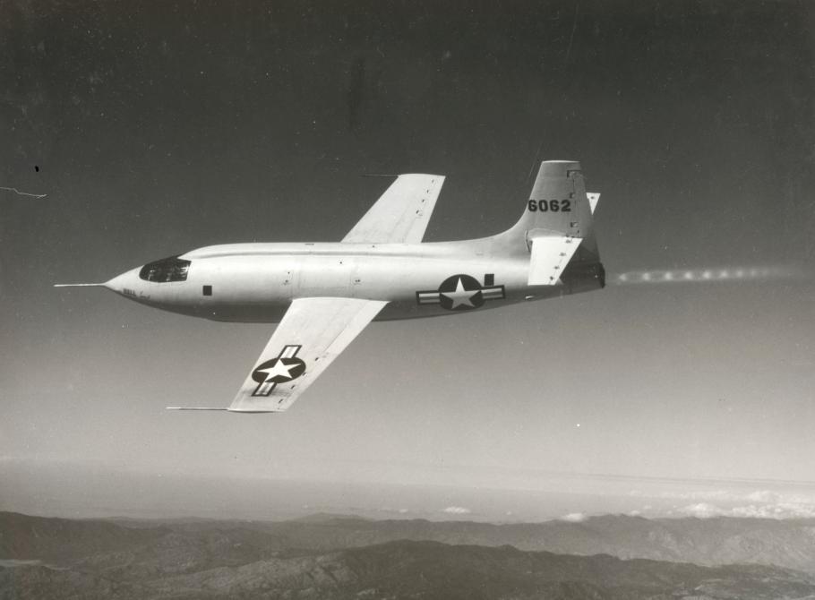 Side view of light-colored aircraft in flight. Aircraft features multiple U.S. military star inside circle with bar emblems.