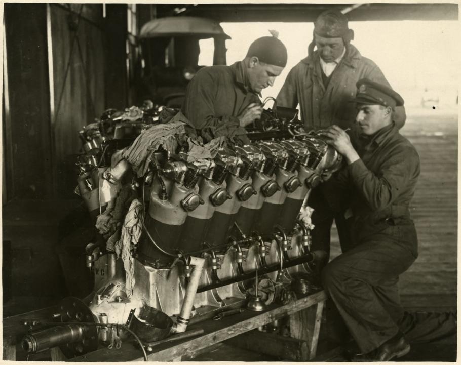 Three people examine a twelve-cylinder engine used for long-travel flight.