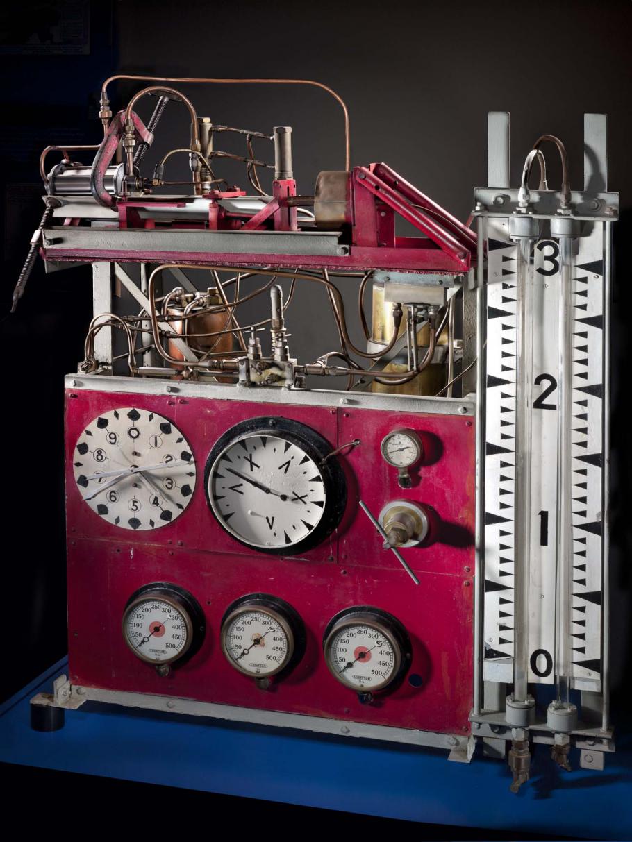 Large table stand with multiple clock-like meters and a large pressure meter. Above the meters are a two-story set of tubes.