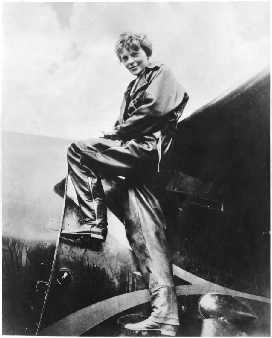 Amelia Earhart, a white woman, climbs into the cockpit of a plane.