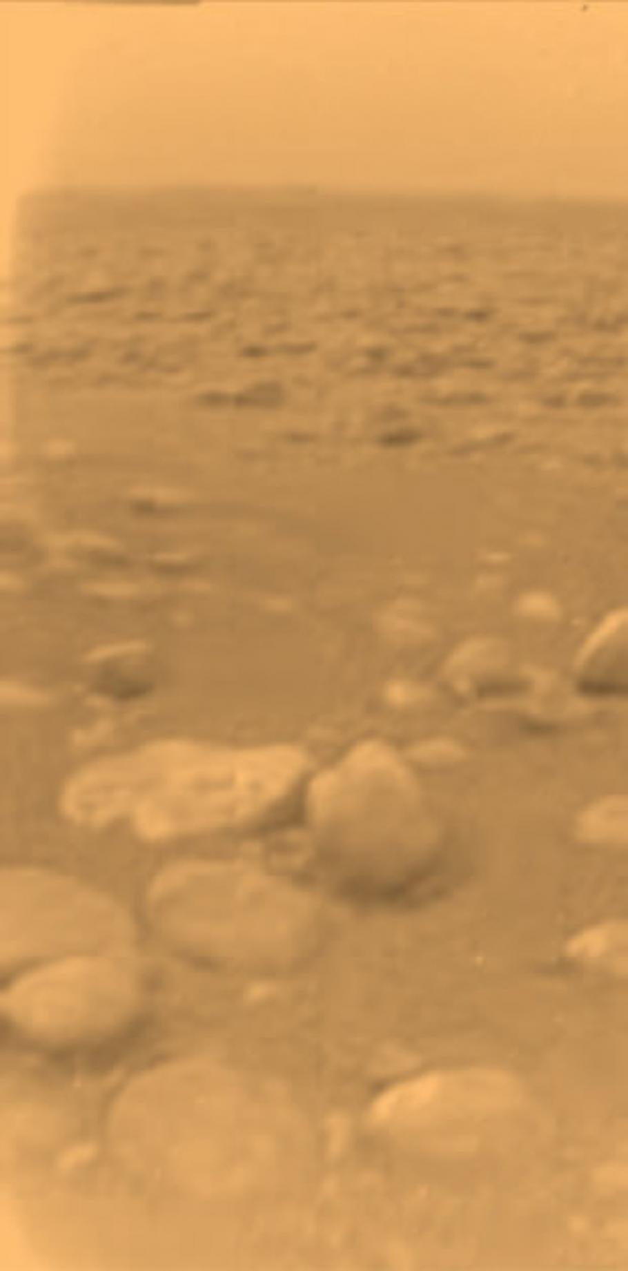 View of a part of the surface of Titan, a moon orbiting Saturn. The visible surface is rocky and is very uneven.