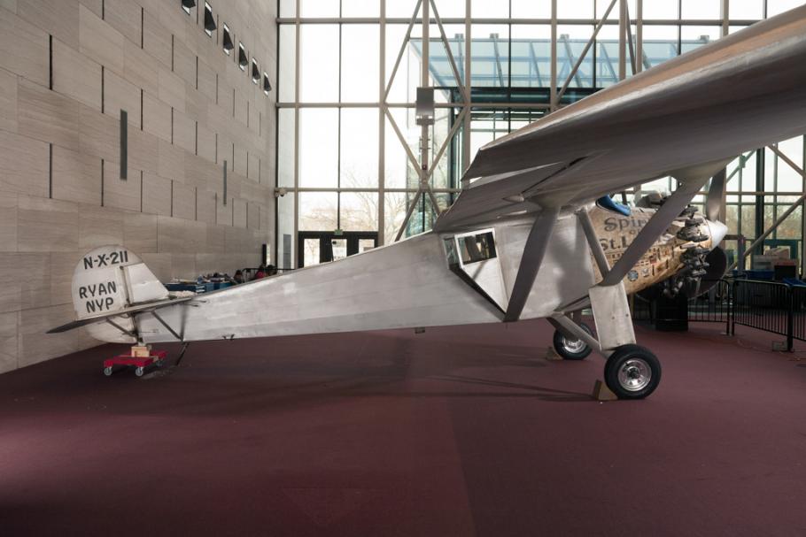 Side view of the Spirit of St. Louis, a silver-colored monoplane, on the floor of the Museum. Registration number "N-X-211" is painted on the tail above the make of the plane, "Ryan MVP".