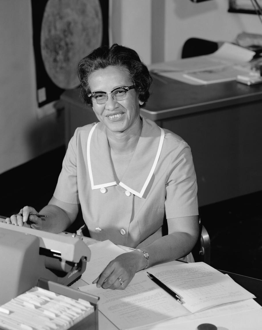 A black and white photo of an African American woman looking up from her desk smiling.