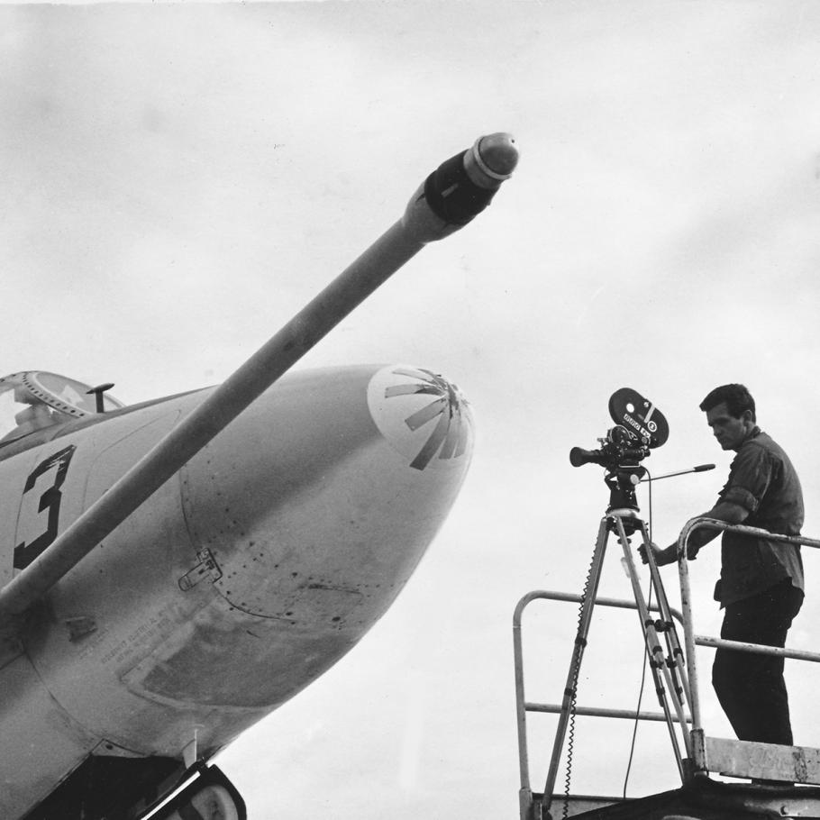 A black and white photograph of a man on a lift filming a battle damaged plane.