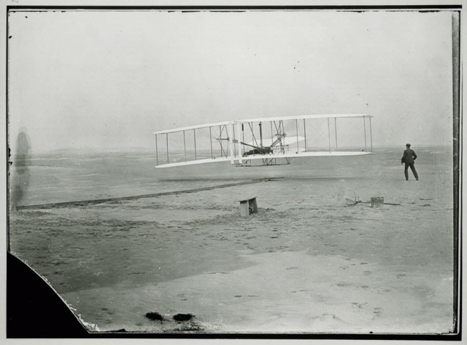 A biplane just barely above the ground with a person standing to the right of it.