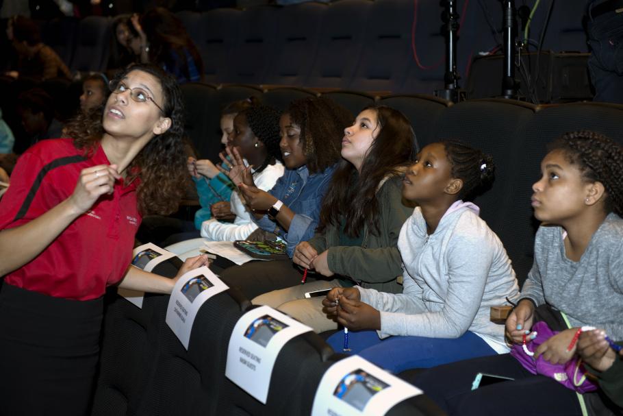 Students in a theater look up at a screen. 