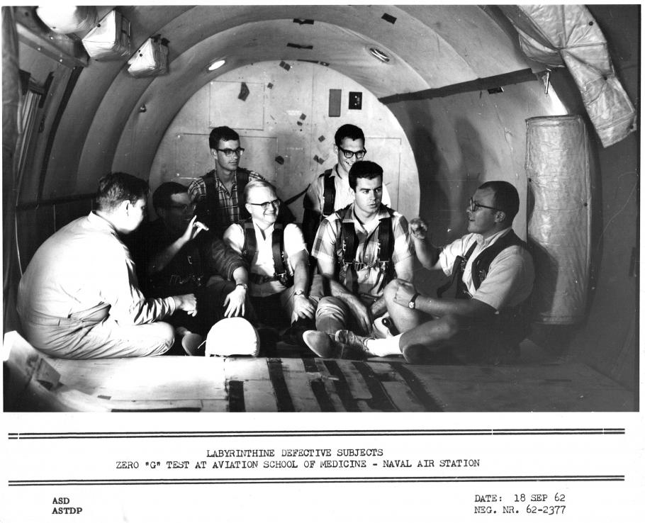 Seven men sit in a tube-like structure. 