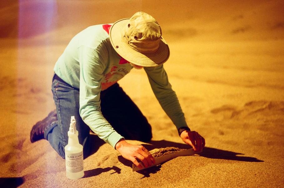 Geologist Jim Zimbelman bends over in the sand with a ruler. 