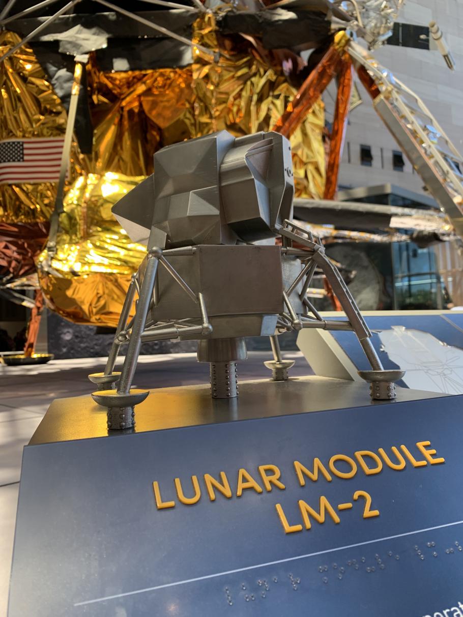 small scale metal version of lunar module with actual lunar module in background