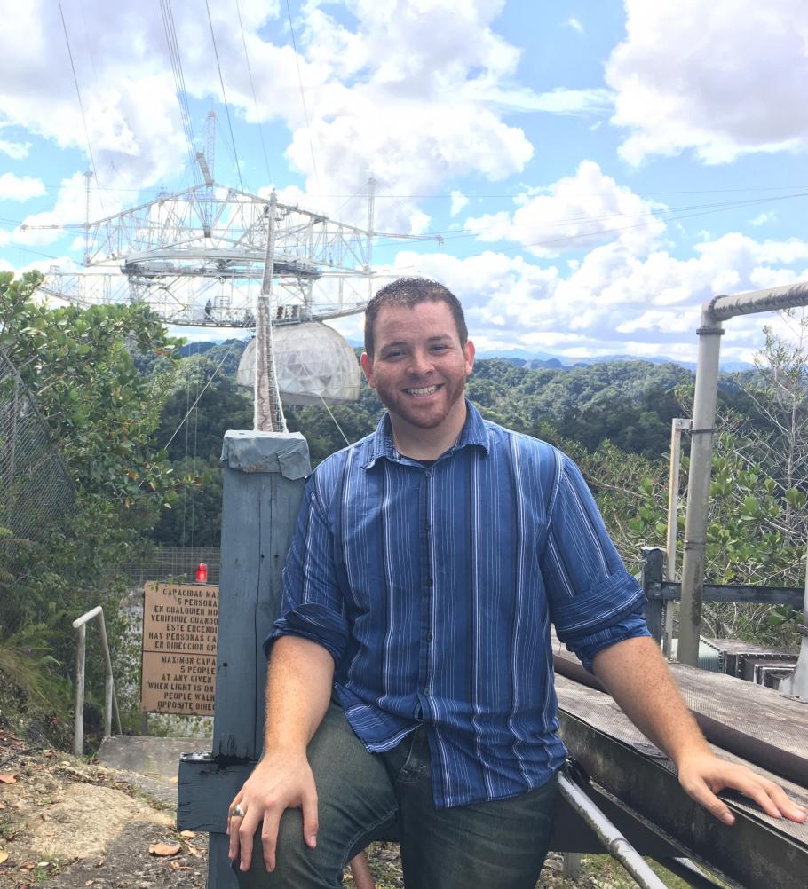 Young person posing for picture with Arecibo Observatory in the background