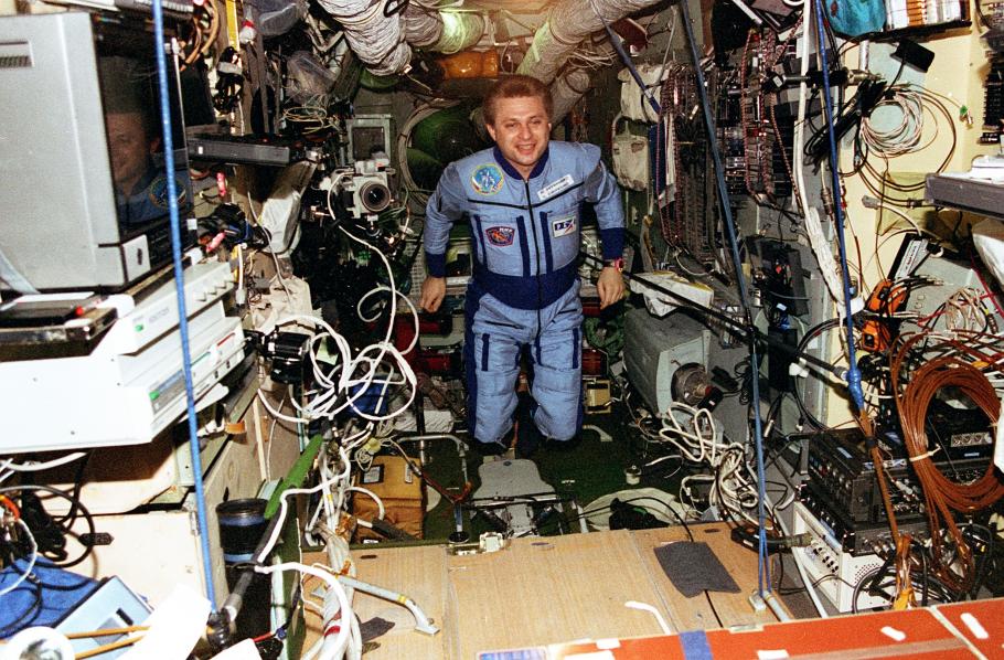 An astronaut floats inside the Mir Space Station, wires and tools float messily around him. 