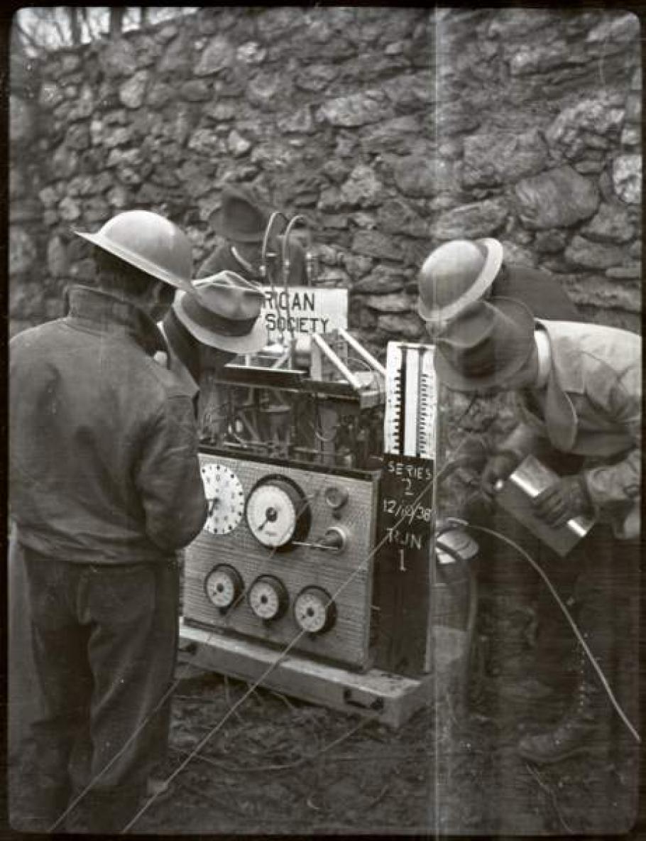 Black and white image of men in helmets working on a motor.