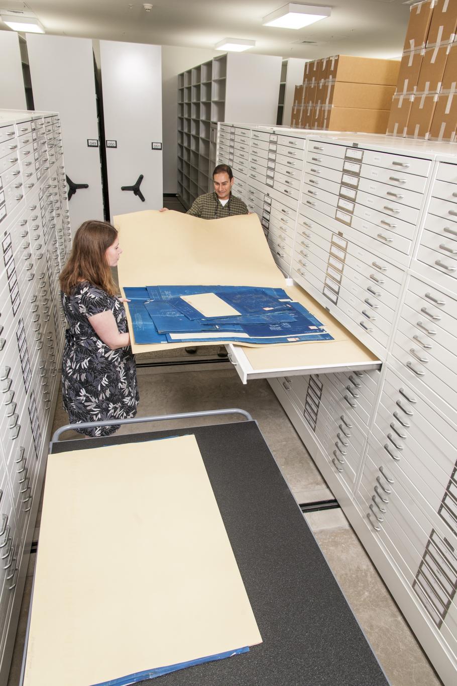 A photo of archivists placing drawings in custom folders and storage.