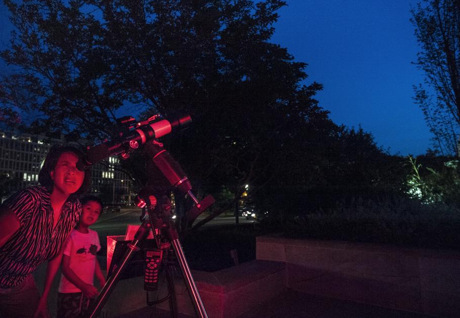 A mother and son use a telescope at night. 
