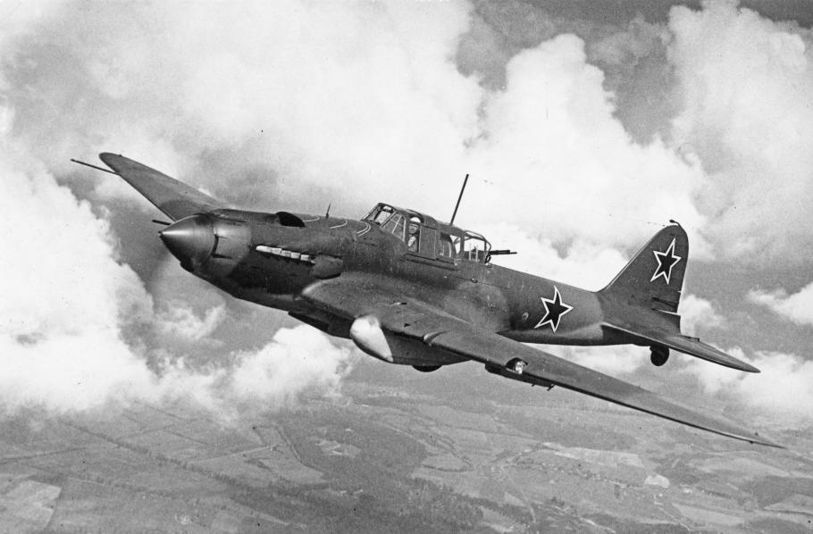 Historical photo of aircraft in flight. Clouds and farmland can be seen in the background. 
