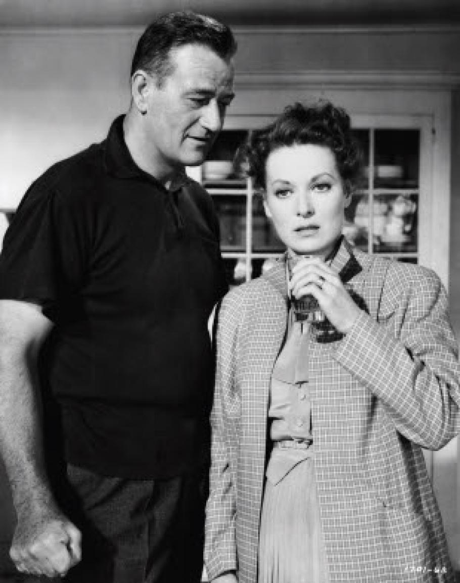 John Wayne stares at Maureen O'Hara while she's on the phone in this film still.
