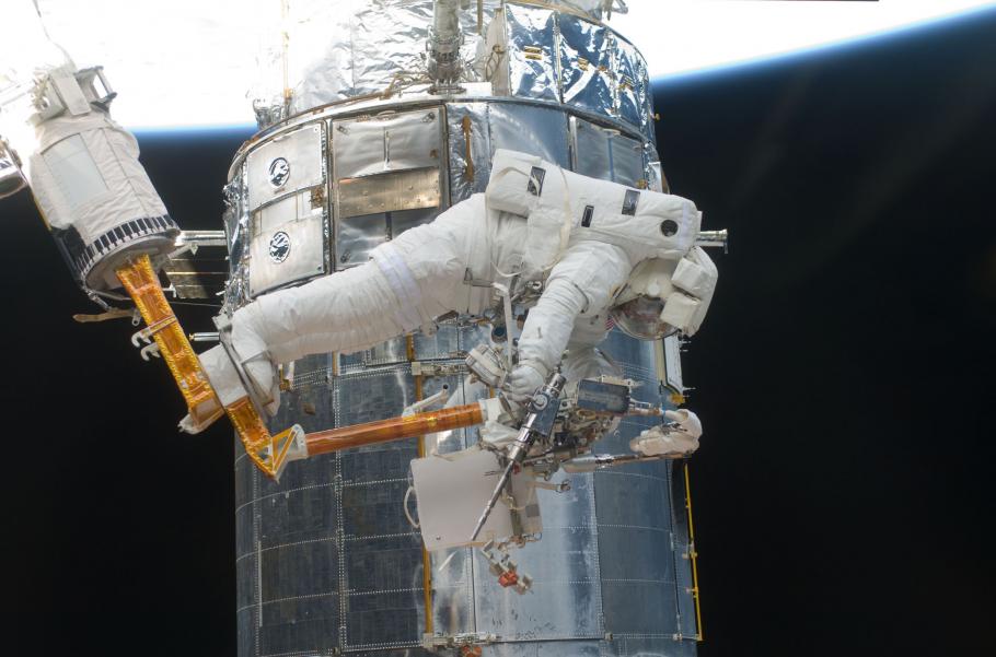 An astronaut during a spacewalk retrieves an object. The astronaut is in a partially prone position.